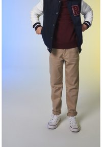 Tummansininen ja valkoinen yliopiston takki, jossa on vaakuna, viininpunainen villapaita, vaaleat chinot ja valkoiset lenkkarit, joissa on purppuranvärisiä yksityiskohtia. Housuissa käännetyt hihansuut.