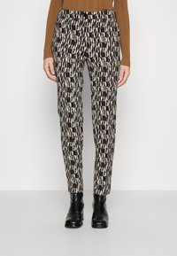 Zwart-witte gestreepte broek met een smal ontwerp. De stof is glad; heeft bruine accenten en een klassieke tailleband. Gedirigeerd met zwarte enkellaarsjes.
