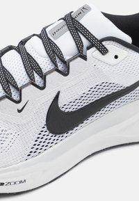 Bijela atletska tenisica s crnim detaljima, mrežastim gornjim dijelom i teksturiranom potplatom. Ima crne vezice i istaknuti Nike logo sa strane.