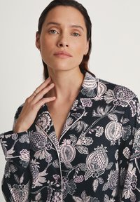 Marineblauw pyjama bovenstuk met bloemen- en fruitpatronen in roze en wit. Gemaakt van een gladde stof met een notch kraag en afgewerkte randen.