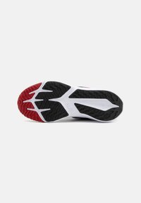 Semelle de chaussure de sport arborant un motif noir et rouge, en caoutchouc texturé pour une meilleure adhérence, et une semelle intermédiaire blanche avec des éléments de design angulaires.