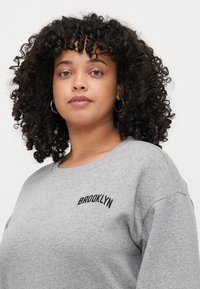 Gray sweatshirt with a rounded neckline and embroidered "BROOKLYN" in black on the left chest area. Soft fabric and relaxed fit.