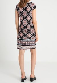 Robe noire à motifs avec des manches courtes, des motifs floraux en rose et bleu, et un ourlet décoratif. Le tissu a une texture lisse.