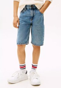 Shorts in denim blu chiaro, taglio comodo e diritto; indossati con sneakers bianche e calzini a righe. Tessuto testurizzato, design casual.