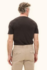 Mustaa puuvillaa oleva istuva t-paita, jossa on lyhyet hihat, yhdistetty beigenvärisiin chinoihin, joissa on takataskut ja napit yksityiskohtina. Näkymä takaa.