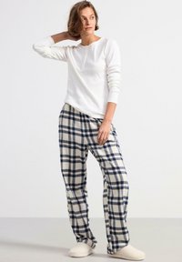 Vit långärmad henley-topp som är kombinerad med byxor i navy och gräddfärgad rutigt flanell. Mjuk textur, avslappnad passform och ljusa tofflor.