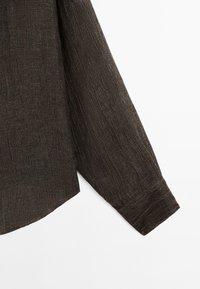 Manche de chemise marron, texturée, avec un léger éclat, présentant un ourlet incurvé et un poignet conçu pour un ajustement ample.