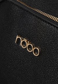 Borsa in pelle nera con texture, dotata di logo e zip in tonalità oro. La vista dettagliata mette in risalto il materiale e i particolari dei metalli.