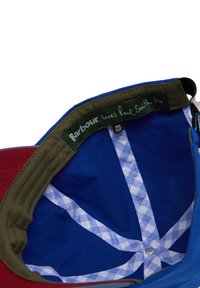 Εσωτερική όψη ενός μπλε και κόκκινου καπέλου με ελιά περιμετρικά, που διαθέτει ετικέτα "Barbour αγαπάει και τον Paul Smith" και ετικέτα με το μέγεθος "one size".