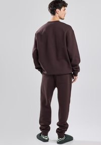 Brown sweatshirt and matching sweatpants made of soft fabric, featuring a relaxed fit and ribbed cuffs, with a back pocket detail.