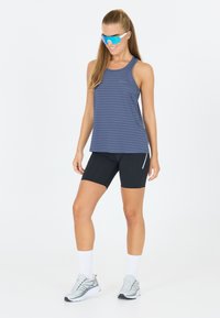 Marine gestreepte tanktop, zwarte shorts en grijze sportschoenen. Model draagt blauwe zonnebril, wat een aangesloten silhouet en sportieve stijl toont.