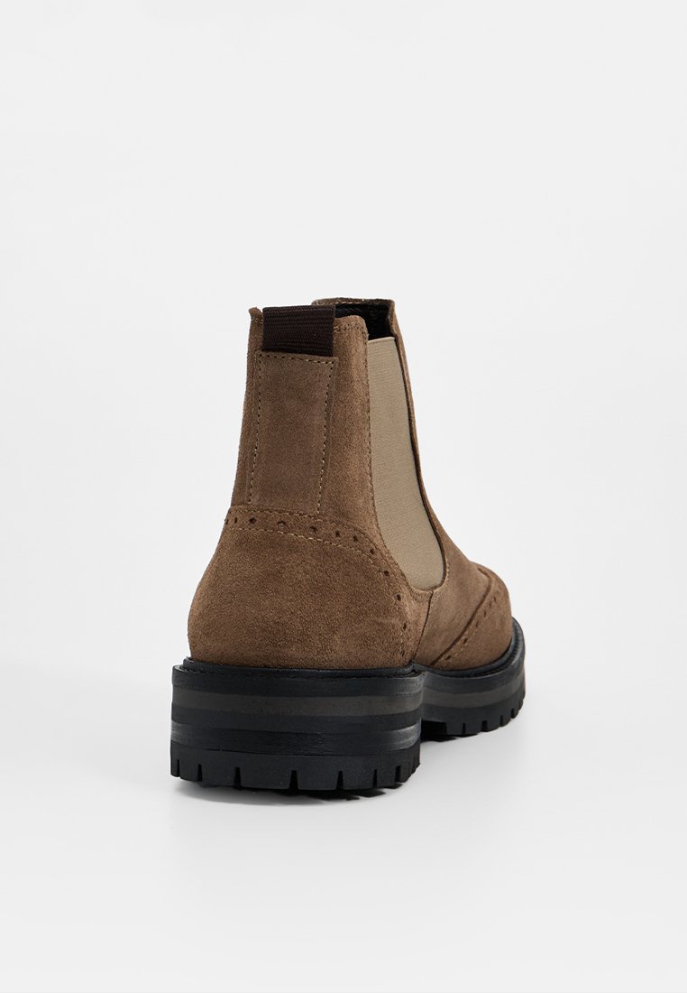 Braune Wildleder Chelsea-Stiefel mit elastischen Seiteneinsätzen, strukturierten Akzenten und einer robusten schwarzen Gummisohle, die mit doppelten schwarzen Streifen versehen ist.