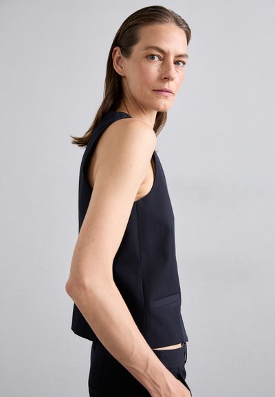 Navy sleeveless top with a tailored fit, round neckline, and side pockets. Minimalistic design with smooth texture and clean lines.