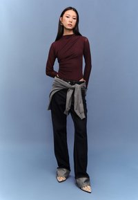 Viininpunainen pitkähihainen yläosa, jossa liehuva malli, harmaa vyötärölle sidottu neule, yhdistetty tummiin farkkuihin ja kärjestä teräväkuvioisiin, täplikkäisiin kenkiin.