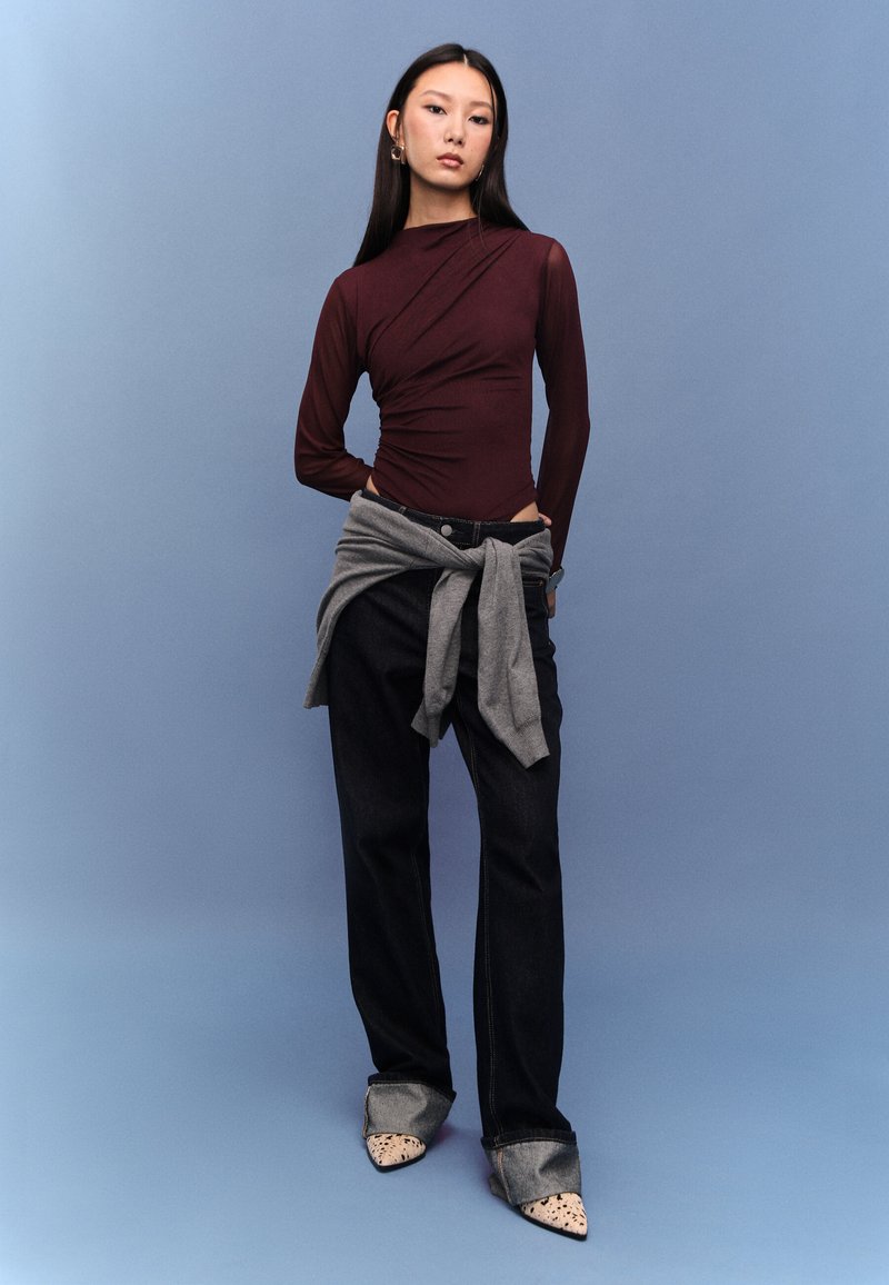 Viininpunainen pitkähihainen yläosa, jossa liehuva malli, harmaa vyötärölle sidottu neule, yhdistetty tummiin farkkuihin ja kärjestä teräväkuvioisiin, täplikkäisiin kenkiin.