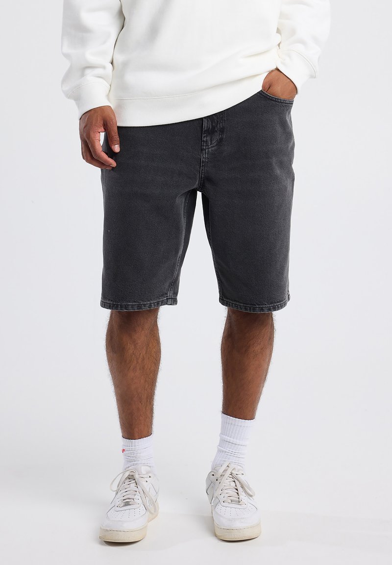 Mustat farkkushortsit suoran leikkauksen kanssa, joissa on viisi taskua ja haalistunut viimeistely, yhdistettynä valkoisiin tennareihin ja nilkkasukkiin.