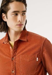 Roestkleurig corduroy shirt met een kraag, knoopsluiting aan de voorkant, een enkele borstzak en subtiele stikseldetails. Klassieke pasvorm en textuur.