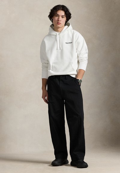 Λευκό βαμβακερό φούτερ με κουκούλα και τσέπη μπροστά, με μαύρο λογότυπο, συνδυασμένο με άνετο μαύρο παντελόνι και μαύρα αθλητικά παπούτσια. Καθημερινό, άνετη εφαρμογή.