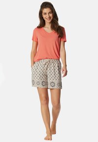 T-shirt corail à col en V associé à un short beige à motifs avec des accents floraux et une taille élastique dotée d'un cordon de serrage.