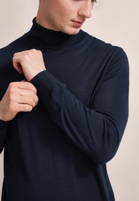 Dunkelblaues Rollkragenpullover mit geripptem Kragen und Bündchen, ausgestattet mit einer weichen, glatten Stricktextur und einer taillierten Silhouette.