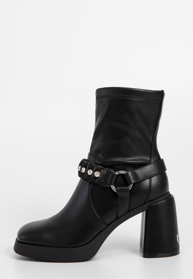 Botas de tobillo negras hechas de cuero sintético, con un tacón bloque, una correa decorativa con strass y una silueta suave y elegante.