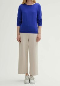 Niebieski sweter o fakturowanej strukturze z długimi rękawami, zestawiony z beżowymi spodniami o szerokich nogawkach z pionowymi szwami. Całość dopełniają białe trampki.