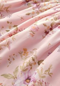 Blommig tyg i mjuk rosa med en jämn textur. Har olika blommönster i pastellfärger, inklusive prästkragar och blad.