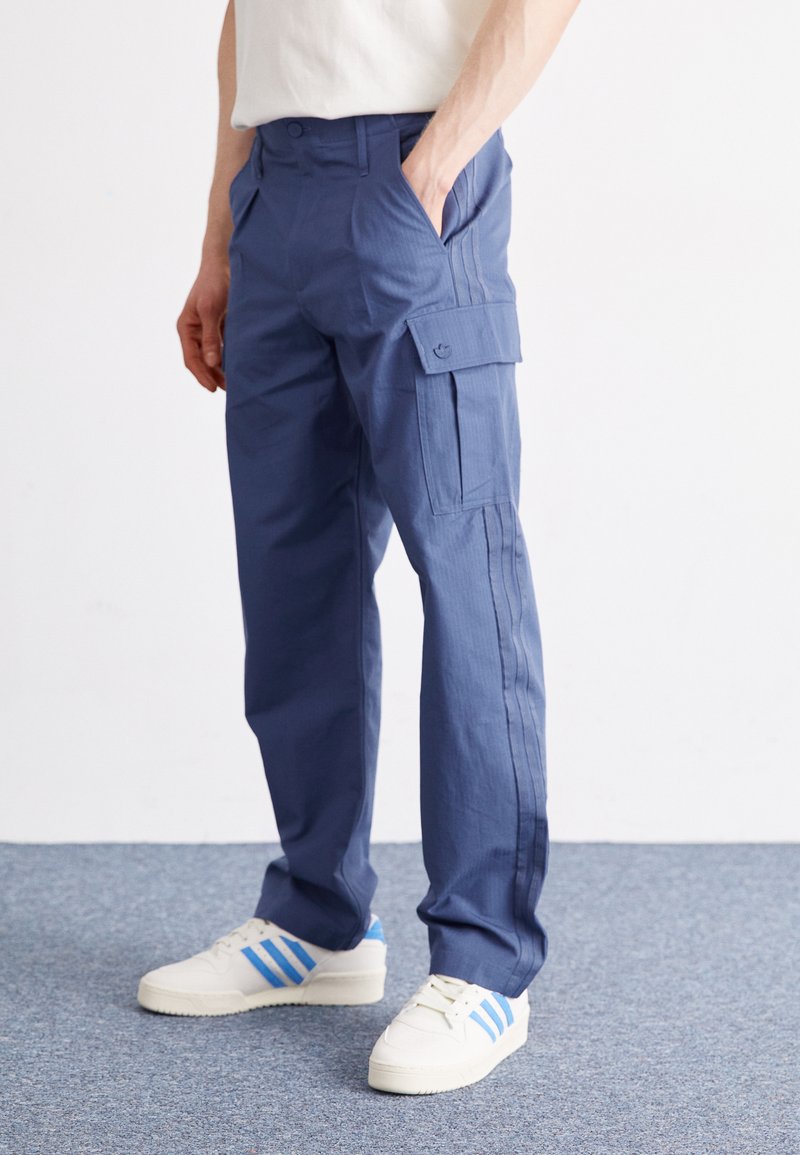 Blauwe cargo broek gemaakt van duurzaam materiaal, met zijzakken, een losse pasvorm en een gladde textuur. Gecombineerd met witte sneakers.