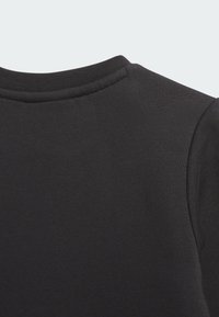 Juoda džemperio medžiaga, rodanti apvalų kaklo iškirpimą ir tekstūruotą paviršių, su matomais siūlių detalėmis ant apykaklės ir peties.