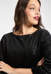 Czarny top z cekinami o dekolcie typu łódka, teksturowanej tkaninie i rękawach do łokcia, ukazujący subtelny efekt połysku.