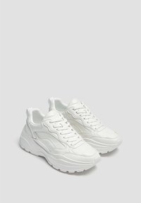 Bílé tenisky vyrobené z hladké kůže, s tlustou, strukturovanou podrážkou, výrazným prošíváním a šněrováním s polstrovaným límcem.