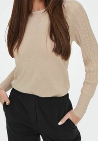 Beige gebreide trui met gestructureerde, patroonmouwen en een ronde hals, gecombineerd met zwarte broek. Comfortabele pasvorm met een casual ontwerp.