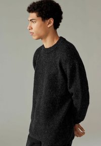 Schwarz gestrickter Pullover in lockerer Passform mit runder Ausschnitt und strukturiertem Finish. Hat lange Ärmel und ein schlichtes Design.