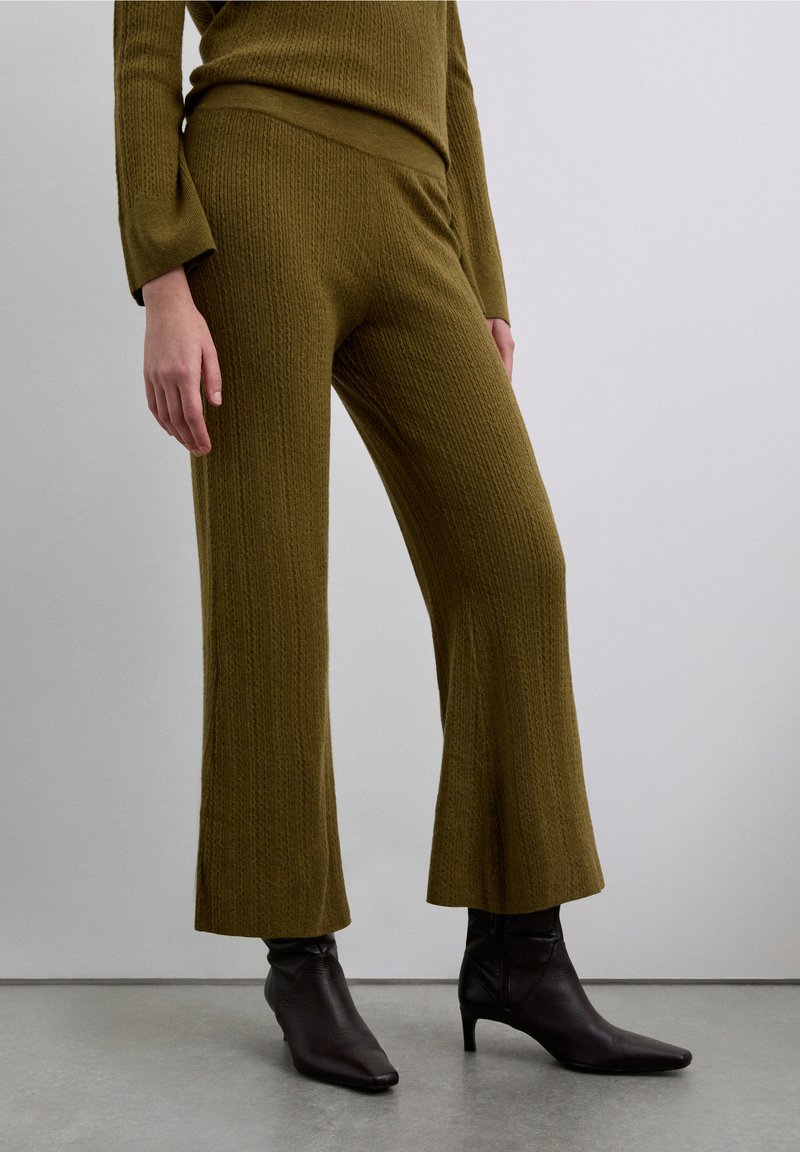 Olive green ribbed knit pants with a flared hem, paired with black pointed ankle boots. Simple waistband; textured fabric throughout.