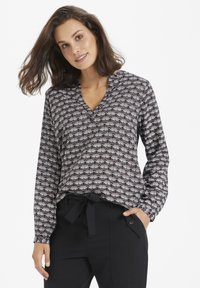 Blusa nera con scollo a V, maniche lunghe e un motivo a ventaglio ripetuto in bianco e rosso. Abbinata a pantaloni neri sartoriali con fiocco.