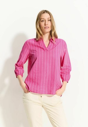 Blusa rosa a righe con scollatura a V e maniche a tre quarti. Il tessuto sembra leggero e leggermente testurizzato, con una vestibilità comoda.