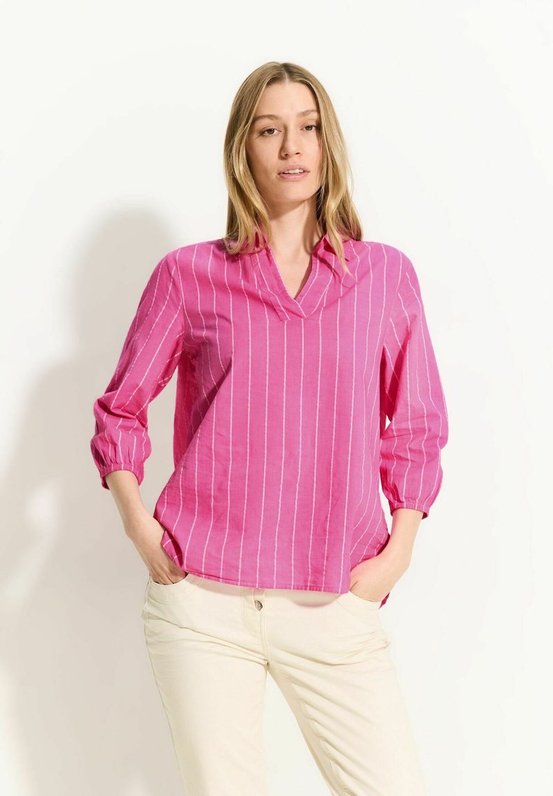 Blusa rosa a righe con scollatura a V e maniche a tre quarti. Il tessuto sembra leggero e leggermente testurizzato, con una vestibilità comoda.