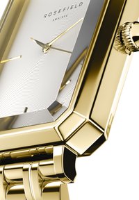 Reloj de pulsera rectangular en tono dorado con una esfera plateada texturizada, marcadores de hora minimalistas y una pulsera de eslabones pulidos. Presenta una corona texturizada.