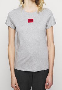 Grå bomulds t-shirt med rund hals og opsmøgede korte ærmer. Har en rød, rektangulær lapp med "HUGO" logo på brystet.