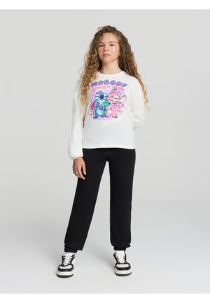 Camicia bianca a maniche lunghe con grafica di cartoni animati colorata che rappresenta due personaggi, abbinata a pantaloni della tuta neri e sneakers bianco e nere.