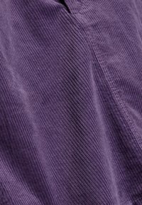 Gros plan sur un tissu en velours côtelé violet montrant des nervures verticales et des détails de couture.