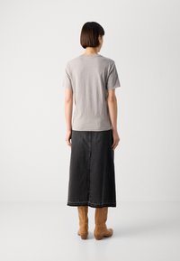 Graues T-Shirt mit kurzen Ärmeln, kombiniert mit einem langen schwarzen Jeansrock und hellbraunen kniehohen Stiefeln, mit geradem Schnitt und minimalistischem Design.