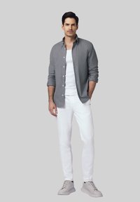 Szara koszula z guzikiem, biały t-shirt, białe spodnie i szare sneakersy; koszula ma podwinięte rękawy i luźny fason.