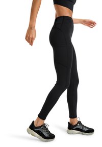 Zwarte leggings van een gestructureerde stof, hoge tailleband en zijzakken, gecombineerd met zwart-grijze sportchoenen met reflecterende accenten.
