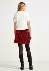 Hvid kortærmet top med tekstureret finish, parret med en rød paljet nederdel. Sættet fuldendes med sorte knæhøje støvler.