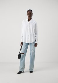 White button-up shirt with long sleeves, paired with light blue ripped jeans. Accessorized with a black handbag and pointed black shoes.
