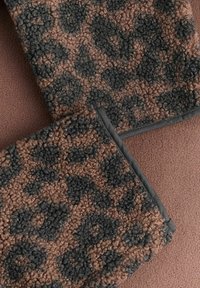 Leopardmønstrete stoff i brunt og svart, med en teksturert overflate og en kontrasterende glatt kant, plassert på en rosa bakgrunn.