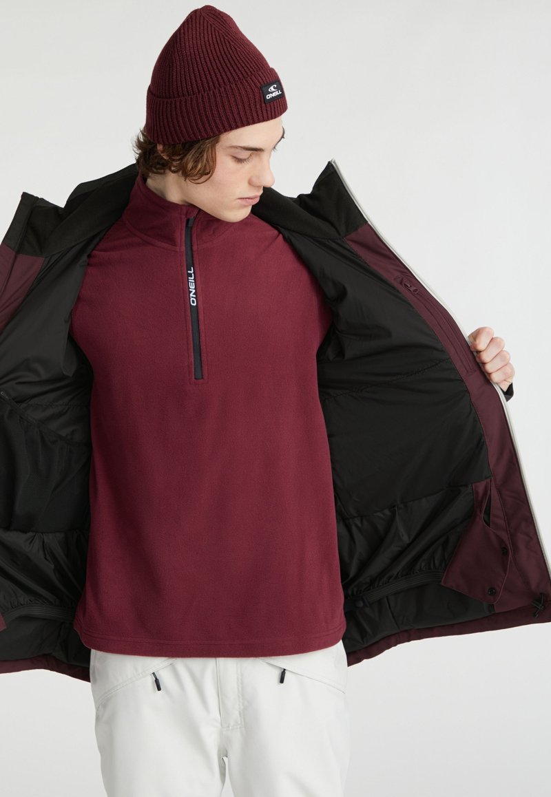 Bordeauxfarbener Fleece-Pullover mit einem halben Reißverschluss und O'Neill-Logo, getragen unter einer schwarzen Jacke, mit glatter Textur und schicht look.