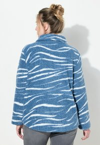 Niebieska polarowa kurtka z białymi wzorami fal, z kołnierzem narzuconym i długimi rękawami. Miękka, teksturowana tkanina o luźnym kroju.