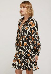 Robe noire avec un motif léopard aux nuances d'orange et de crème. Caractéristiques : un devant à fermeture boutonnée, des manches longues et un design de jupe à volants.